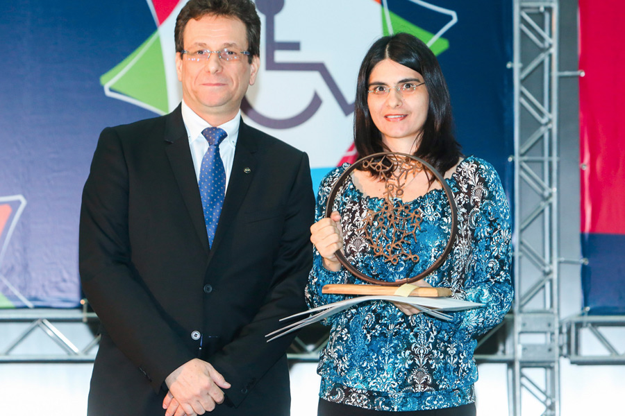 Cláudia Nascimento em destaque segura troféu do prêmio de terceiro lugar.