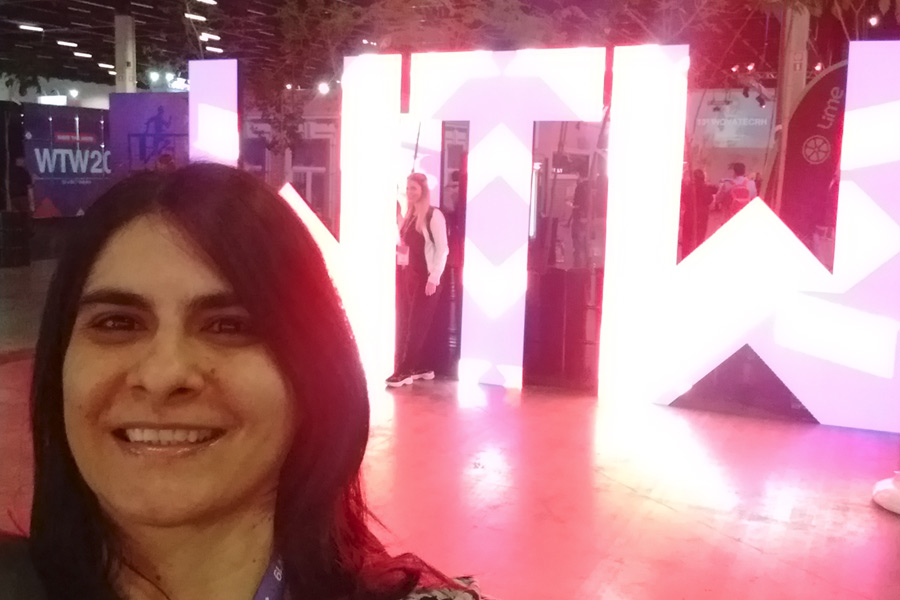 Cláudia Nascimento sorri em destaque em frente ao letreiro luminoso no evento Wellcome Tomorrow.